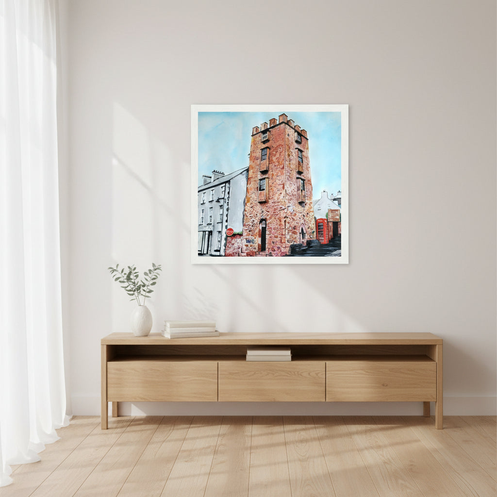 30×30 cm white-framed square art print of The Curfew Tower Cushendall displayed above a console table, bright airy interior, soft white walls, light oak furniture, calm atmosphere, lifestyle home photograph with gentle natural lighting.
