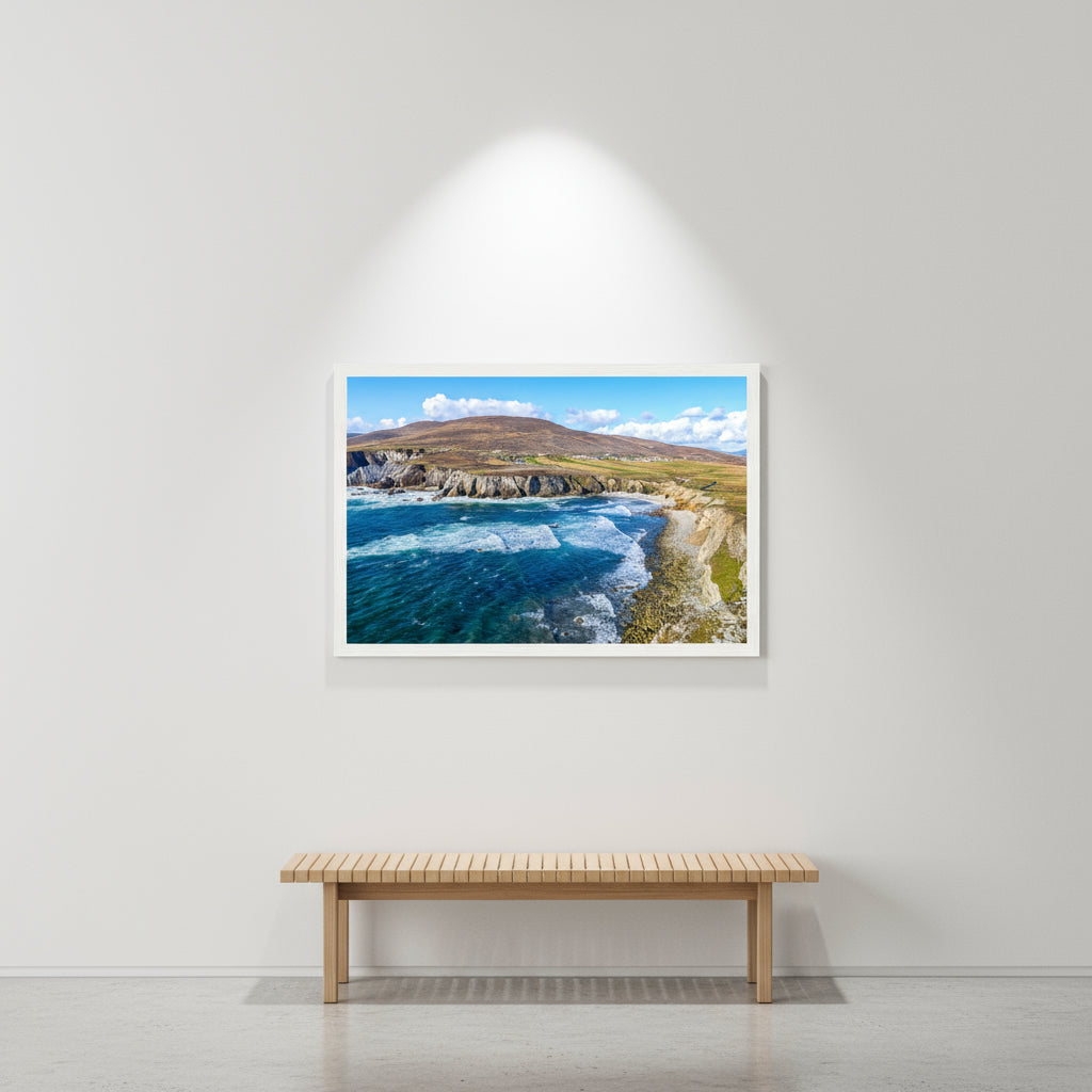 Wood-framed Achill Island print on gallery-white wall, polished concrete floor, spotlight illumination and minimalist bench beneath the artwork.