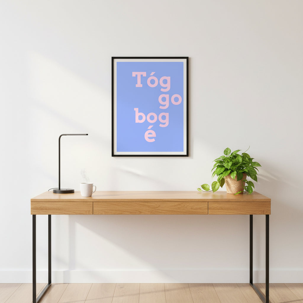 Blue and pink version framed in black, positioned above a sleek oak desk with a ceramic mug, green plant and soft ambient lighting.