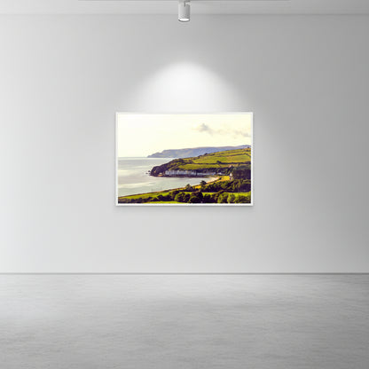 Wood-framed Cushendun print on gallery-white wall with subtle spotlighting and polished concrete floors.
